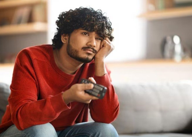 Young man looking bored holding TV remote – Best Psychiatrist for Gaming Addiction in Vijay Nagar